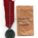 Ostmedaille mit Verleihungstüte, Winterschlacht im Osten 1941/42 (Hst. 28 – Eugen Schmidhäussler, Pforzheim) mit 20 im Bandring markiert)